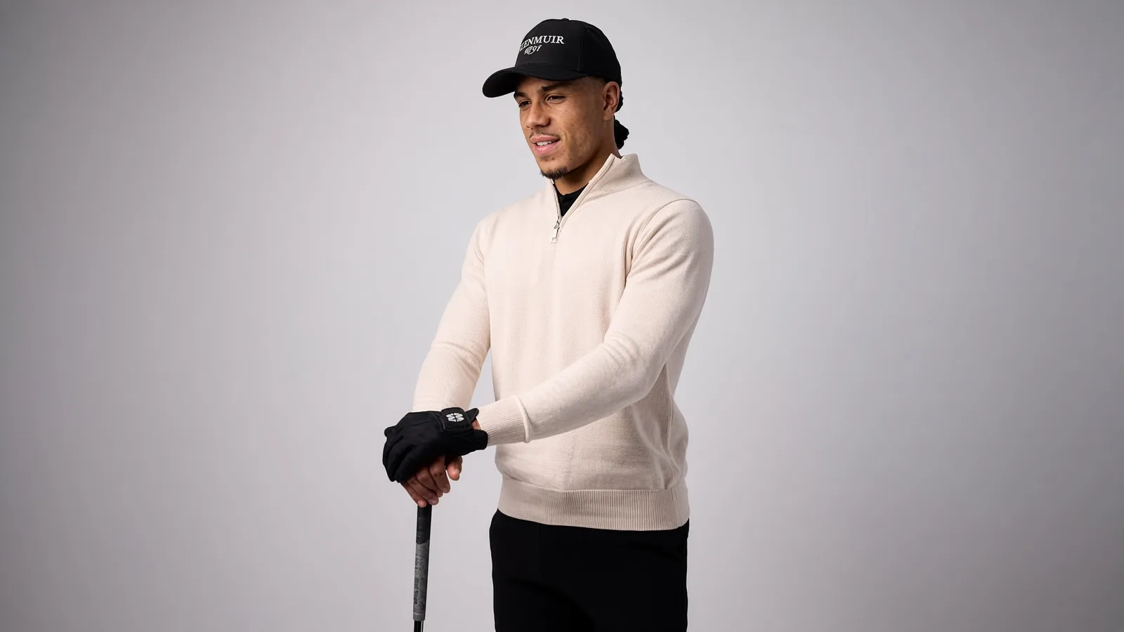 Golfer wearing a cream quarter-zip knit midlayer over a black base layer, gripping a club