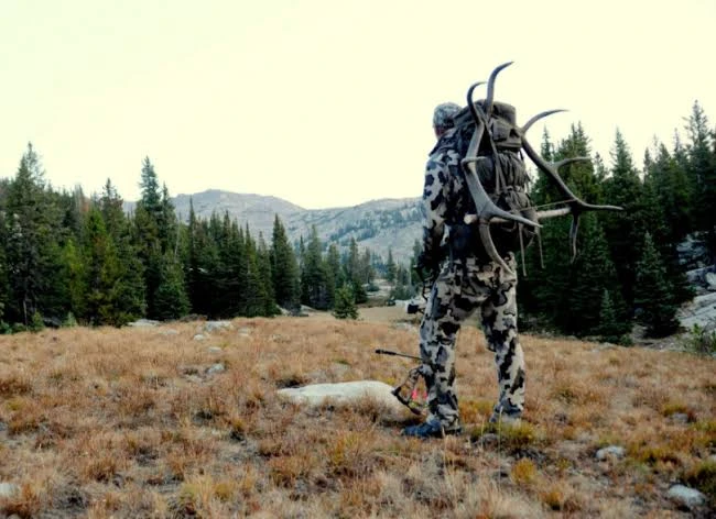 Backcountry hunter glassing across alpine big game terrain — extreme-weather layering system testing