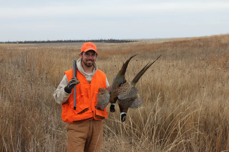 Upland bird hunter working through tall CRP grass with pointing dog — brush-tested hunting apparel