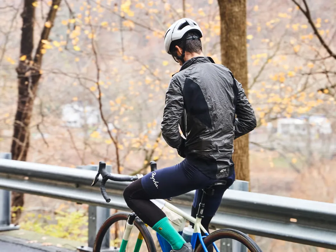 Cyclist in a black packable rain jacket zipping up over bib tights on a wet autumn road