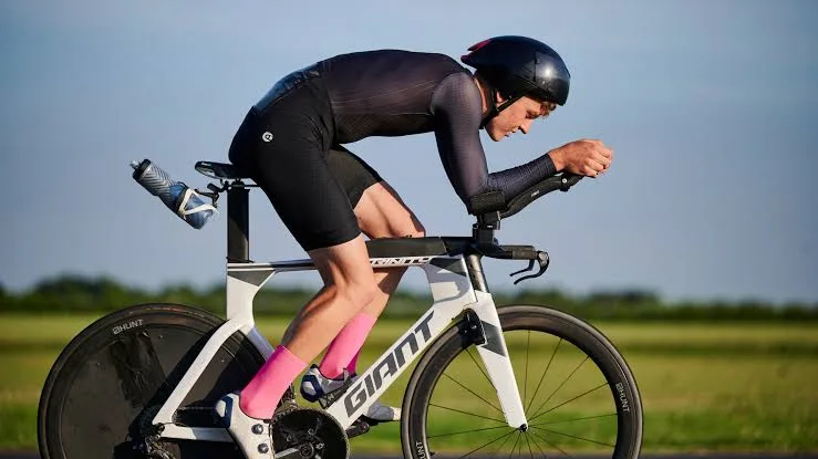 Rider in a black long-sleeve cycling skinsuit on a time trial bike with aero bars and a disc wheel