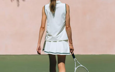 White sleeveless performance tennis polo with a structured piqué collar, worn on court with a pleated skirt and racket